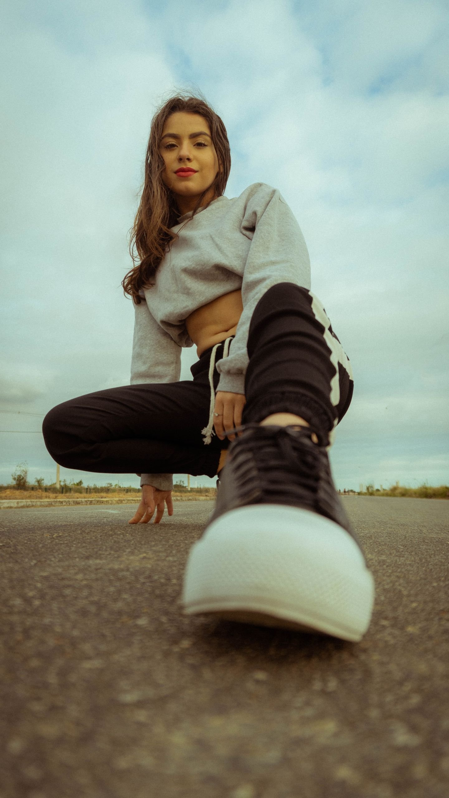 Young woman crouching playfully on asphalt, showcasing casual urban fashion with a unique perspective.